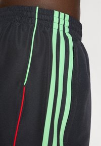 Černé sportovní šortky s lehkým materiálem, elastickým pasem a zelenými a červenými pruhy po stranách pro zvýraznění.