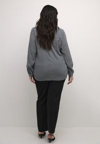 Long-sleeve blouse in black and white geometric pattern, featuring a loose fit and gathered cuffs. Paired with black trousers and heels.