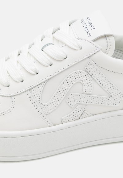 Sneaker bianco in pelle con finitura liscia, dettagli del logo perforato prominente, lacci bianchi piatti e suola in gomma spessa e texturizzata.