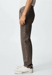 Jeans in denim marrone a taglio slim, con vita a media altezza e classico design a cinque tasche. Indossati con sneakers bianche.