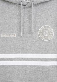 Šedá mikina s kapucí a šňůrkami, bílé horizontální pruhy, obdélníková nášivka s nápisem "UNFAIR ATHL" a kulatý emblém s nápisem "UNFAIR CREW, DON'T MESS WITH US."