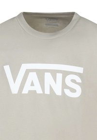 Camiseta beige con cuello redondo que presenta un destacado logo en blanco de "VANS" en letras grandes y en bloque en el pecho. Textura de tela suave.