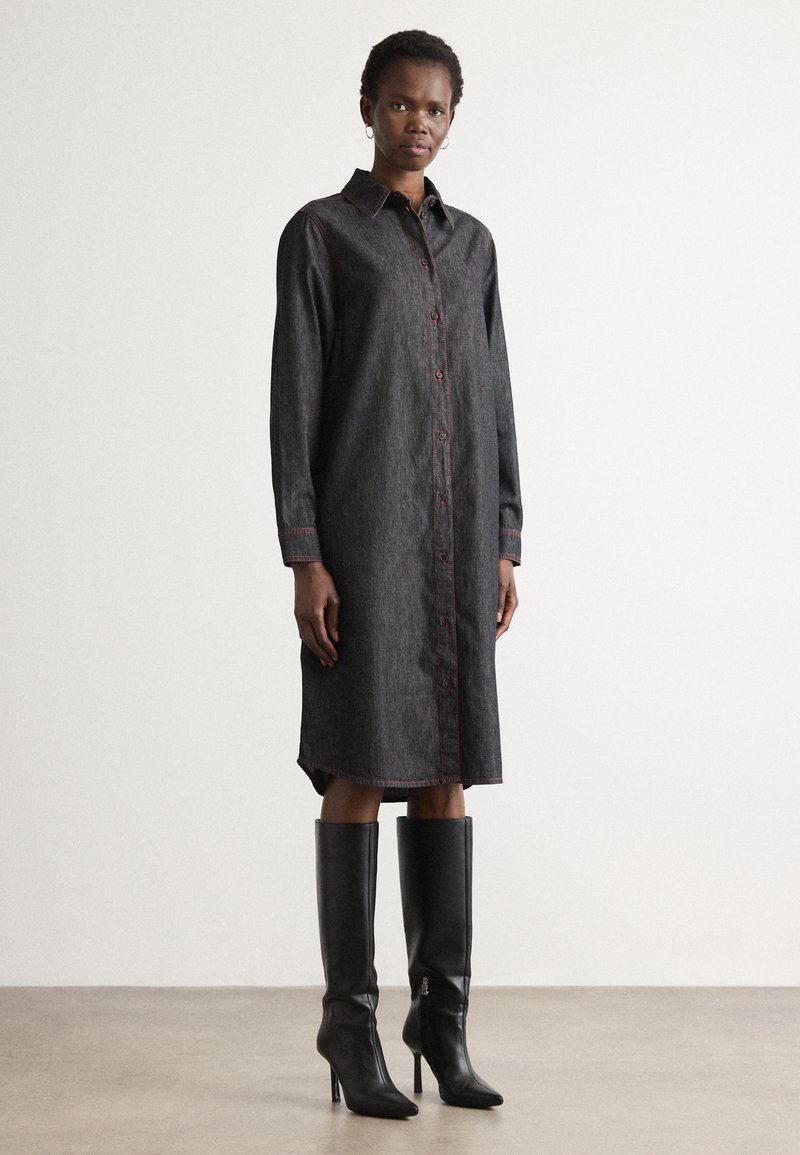 Dunkelblaues Jeanshemdkleid mit Knopfleiste, langen Ärmeln und roten Nähten. Kombiniert mit kniehohen schwarzen Stiletto-Stiefeln. Glatte Textur.