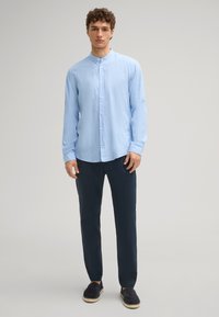 Camicia a maniche lunghe di colore blu chiaro con colletto, chiusura a bottoni e tessuto texturizzato, abbinata a pantaloni blu navy e scarpe espadrilles nere.