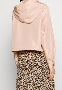 Skórzana, jasnoróżowa kurtka z kapturem, z długimi rękawami i gładką teksturą, w zestawie z spódnicą w szary nadruk w panterkę.