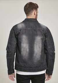 Juodas džinsinis švarkas su nuvarytu paviršiumi, briaunotais detalėmis ant pečių ir mygtukų uždarymu ant rankovių. Sukurtas lieknam siluetui.