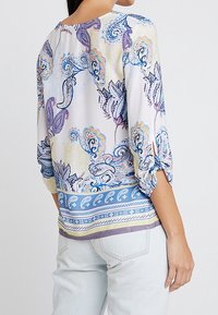 Blouse multicolore avec un motif floral et cachemire, à manches 3/4 et un design à fond élastique en nuances de bleu et de violet.