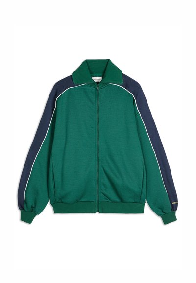 Zeleni i tamnoplavi zip-up jakna s bijelim detaljima, rebrastim manžetama i ovratnikom. Ima opuštenu kroj i mekani, teksturirani materijal.