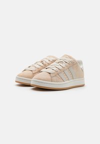 Light beige sneakers made of suede and leather, featuring textured accents, flat laces, perforated toe, and a white rubber sole.