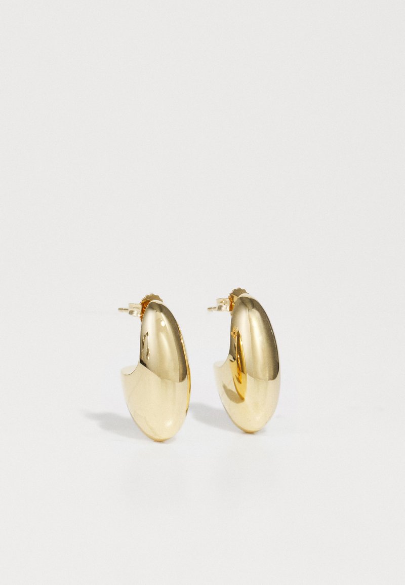 Zelta riņķa auskari ar gludu, noapaļotu dizainu, atstarojošu virsmu un drošu aizdari.