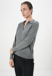 Pullover grigio a maglia con maniche lunghe, scollo a V e colletto, poggiato su un pantalone nero a vita alta. Marchio sottile vicino all'orlo.