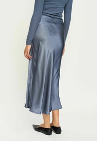 Satin, knælang nederdel i skiferblå med en let glans, med et flydende design og subtilt prikkemønster. Kombineret med sorte flade sko.