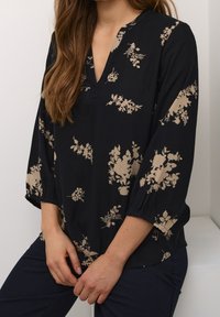 Blusa negra con estampado floral, de mangas tres cuartos, con escote en V y un patrón floral en beige. El material parece ligero y texturizado.