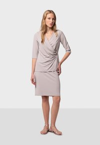 Robe enveloppante gris clair avec des manches trois-quarts, des détails froncés à la taille et une jupe mi-longue. Associée à des sandales argentées.