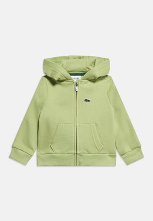 Vaaleanvihreä hupullinen vetoketjutakki, jossa on etutaskut, huppu, resorit hihansuissa ja pieni kirjailtu krokotiililogokuva rinnassa.