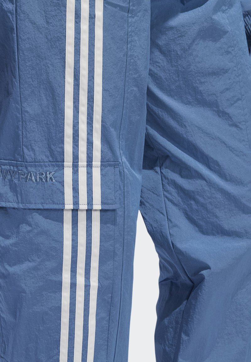 Blauwe cargobroek van lichtgewicht materiaal met drie witte verticale strepen aan de zijkanten en een geborduurd logo op de zak.