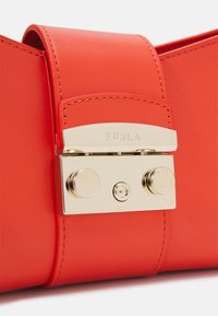 Sac à main en cuir rouge avec quincaillerie dorée, fermeture à rabat et détails de couture visibles. Nom de la marque "Furla" embossé sur le fermoir.