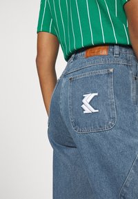 Jeans i ljusblå denim med rak skärning, med en läderlapp i midjan och en vit broderad logotyp på bakfickan.