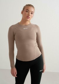 Beige pikkade varrukatega topp, sobiv disain pehme tekstuuriga. Omab ümmargust kaelust ja "aimn" logo rinnal. Mustad legginsid kuuluvad komplekti.