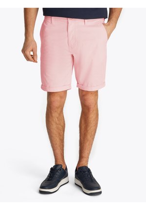 Shorts rose clair avec un devant plat, des ourlets roulés et des passants de ceinture. Portés avec des baskets bleu marine avec une semelle blanche.