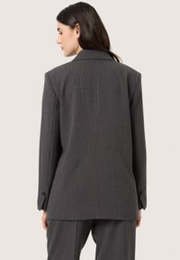 Grå stribede blazer med strukturerede skuldre og en enkelt knap ved manchetten; stoffet har en glat tekstur og et klassisk skræddersyet design.