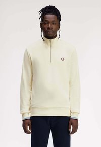 Felpa con zip color crema con collo alto e polsini a coste, con un piccolo logo ricamato sul petto. Tessuto morbido.