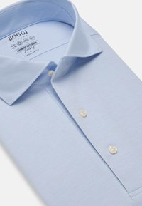 Svetlo modra srajca z gumbi, bombažna tkanina, običajen kroj, špičast ovratnik, dva bela gumba, oznaka blagovne znamke vidna znotraj ovratnika.