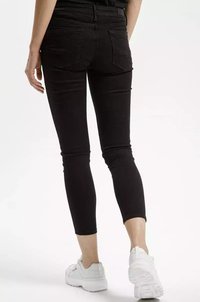 Czarne dopasowane dżinsy o średnim stanie, z tylnymi kieszeniami i dopasowanym krojem, w połączeniu z białymi sportowymi butami.