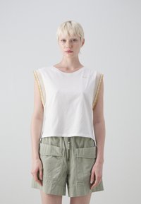 Hvitt bomulls crop-top med bølgete gule og beige detaljer på ermene, kombinert med olivengrønne shorts med store frontlommer.