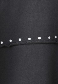 Tissu gris foncé avec une rangée horizontale de petits boutons ronds blancs au-dessus d'une couture tricotée décorative.