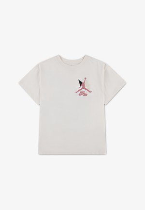 T-shirt blanc à manches courtes avec un logo graphique Nike Air et Jumpman rouge sur la poitrine gauche, décoré de formes géométriques.