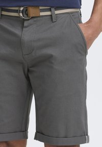 Pantalones cortos grises de tejido entrelazado, con dobladillo enrollado, bolsillos laterales y un cinturón de rayas en contraste con un acento de cuero marrón.