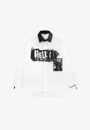 Hvid skjorte med lange ærmer og en krave af sort læder. Fronten har fed tekst "HEJ, JEG ER ROCK" og en lomme med et guitargrafik. Tekstureret stof.