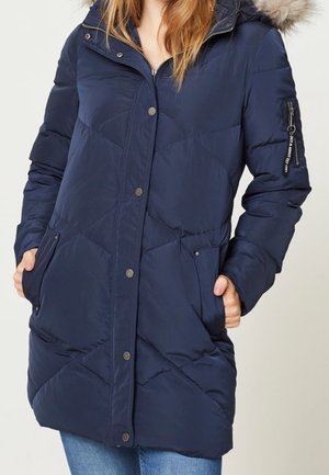 Doudoune bleu marine avec design matelassé, capuche doublée de fourrure, poche latérale zippée et fermeture à pressions, avec deux poches avant.