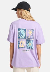 Lys lilla oversized t-shirt med et grafisk design, der viser fire firkanter. Hver firkant har farverige mønstre og teksten "BILLABONG" nedenfor.