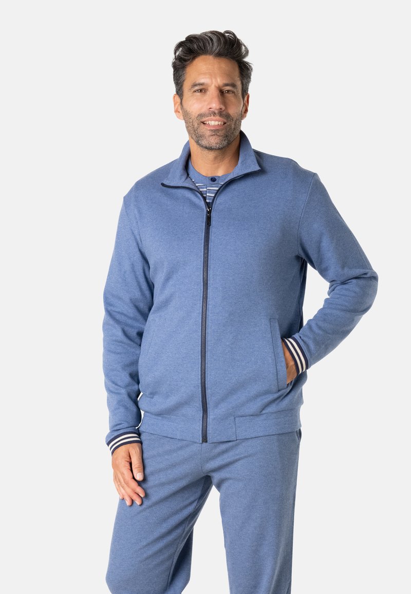 Veste zippée bleue pour homme en matière douce avec poches latérales, poignets côtelés aux rayures blanches et bleu marine, associée à un pantalon assorti.