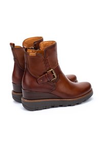 Bottes ankle en cuir marron avec un détail tissé, une boucle sur le côté et une semelle en caoutchouc texturée. L'intérieur est beige et cousu pour le confort.
