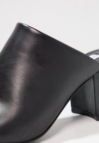 Zwarte leren muiltjes met een ronde voorkant, taps toelopende hak en een gladde textuur. Heeft een solide ontwerp met een lichte glans.