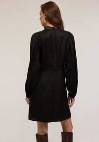 Schwarzes Kleid mit strukturiertem Stoff, puffärmel und einem hohen Spitzenkragen. Das Design umfasst eine taillierte Taille und einen knielangen Saum.