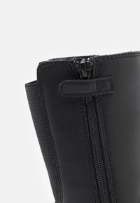 Bottines en cuir noir avec fermeture à glissière, panneaux élastiques sur les côtés et détails de couture, avec une texture lisse et une finition mate.