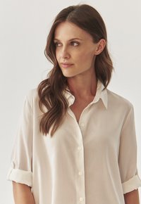 White button-up shirt made of lightweight fabric, featuring a classic collar and rolled-up sleeves for a relaxed fit. Smooth texture.