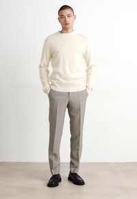 Világos bézs gyapjú pulóver, slim-fit szürke nadrág világos csíkokkal és sötétbarna bőrcipők. Egyszerű, modern dizájn.
