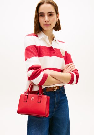 Woman wearing a red and white striped sweater with folded arms, holding a red handbag, and wearing blue jeans and a brown belt.