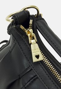 Svart handväska med en blandning av läder och texturerat material, guldfärgad dragkedja och en loggad dragkedja med hjärtdetalj.
