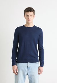 Sötétkék, könnyű pulóver, finom kötött anyagból készült, kerek nyakkal, hosszú ujjakkal és diszkrét logóval a mellrészen.