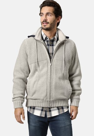 Grauer Reißverschluss-Pullover mit geripptem Muster, gefütterter Kapuze aus Fleece und Seitentaschen, getragen über einem blau karierten Hemd.