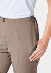 Braune maßgeschneiderte Hosen mit glatter Textur, ausgestattet mit seitlichen Taschen und einer flachen Vorderseite. Der Bund hat einen Metallverschluss.