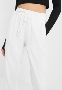 Pantalons blancs en mélange de lin léger avec une taille élastique et un cordon de serrage. Coupe ample. La texture semble douce et respirante.