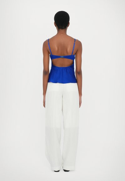 Top senza maniche blu royal con schiena a taglio. Abbinato a pantaloni bianchi larghi e fluidi. Tessuto soffice con spalline regolabili.
