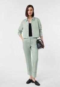 Miętowa, krótka kurtka z dwiema kieszeniami, w połączeniu z pasującymi spodniami. Czarna bluzka, mała czarna torebka i czarne buty dopełniają stylizację.